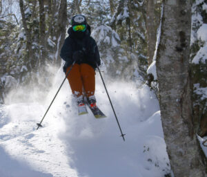 An image of Ty jumping out of exploding powder as he skis a line in the Maria's area at the end of a March storm cycle at Bolton Valley Ski Resort in Vermont