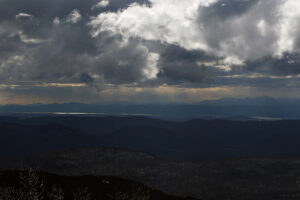 An image of the Adirondack Mountains of New York State beyond Lake Champlain with areas of snow squalls and afternoon light visible in Mid-March take from Bolton Valley Ski Resort in Vermont