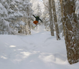 An image of Ty jumping out of the powder snow while skiing in the Sure Shot trees area after Winter Storm Ronnie at Bolton Valley Ski Resort in Vermont