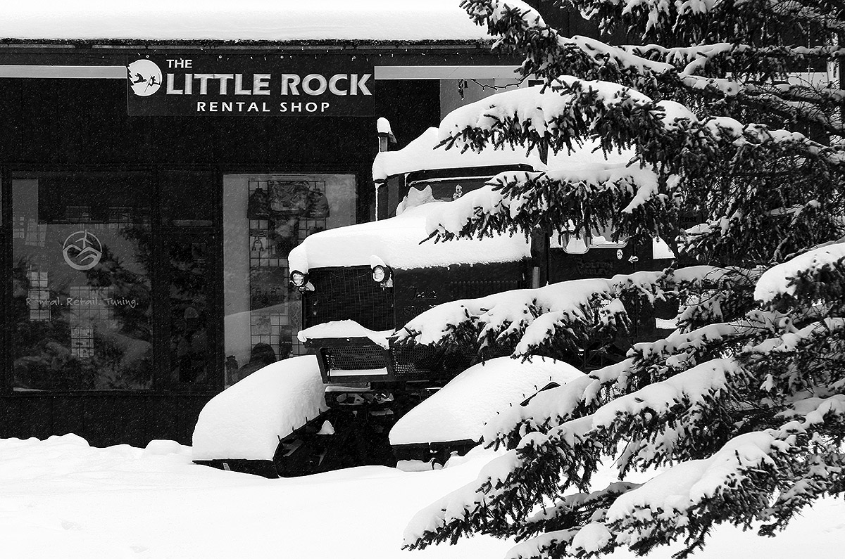 An image of evergreen branches, an old snowcat, and the Little Rock Rental Shop covered in powder from rounds and rounds of early December snow up at Bolton Valley Ski Resort in Vermont