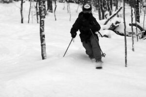 An image of Ty Telemark skiing through trees in the Cup Runneth Over glade as twilight approaches and we near the end of today's ski tour on the Nordic and Backcountry Network at Bolton Valley Ski Resort in Vermont