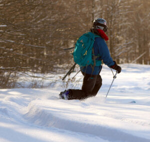 An image taken from behind of Erica Telemark skiing in powder while on a December ski tour at the Timberline are of Bolton Valley Ski Resort in Vermont