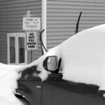 An image of a car covered with drifted snow near parking signs during the windy upslope portion of an early January winter storm cycle in the Village area of Bolton Valley Resort in Vermont