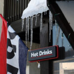 An image of a sign for "Hot Drinks", a flag indicating "Open", and icicles at the Miso Toh Kome food hut outside the main base lodge at Bolton Valley Ski Resort in Vermont