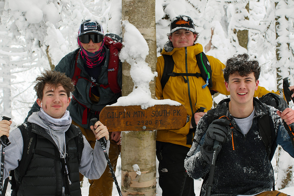 An image of Dylan, Jack, Dylan, and Ronan pausing for a picture at the South Peak of Gilpin Mountain on the Long Trail during a ski tour in the Jay Peak backcountry.